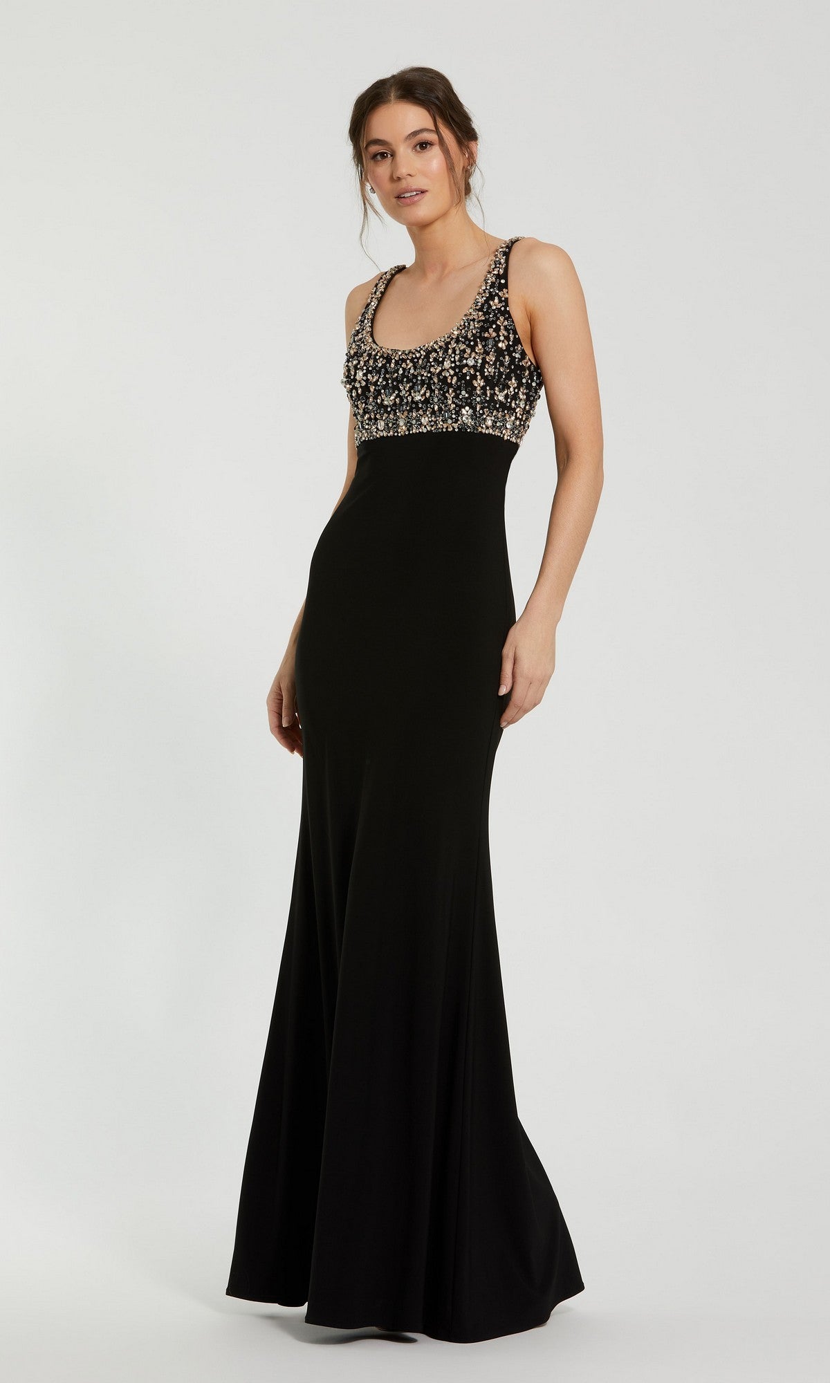 A woman wearing the Mac Duggal 2253 Long Formal Dress in black, featuring a fitted crystal-embellished beaded bodice, sleeveless design, and flared skirt, standing against a plain light background—an elegant choice for evening events or any formal occasion.